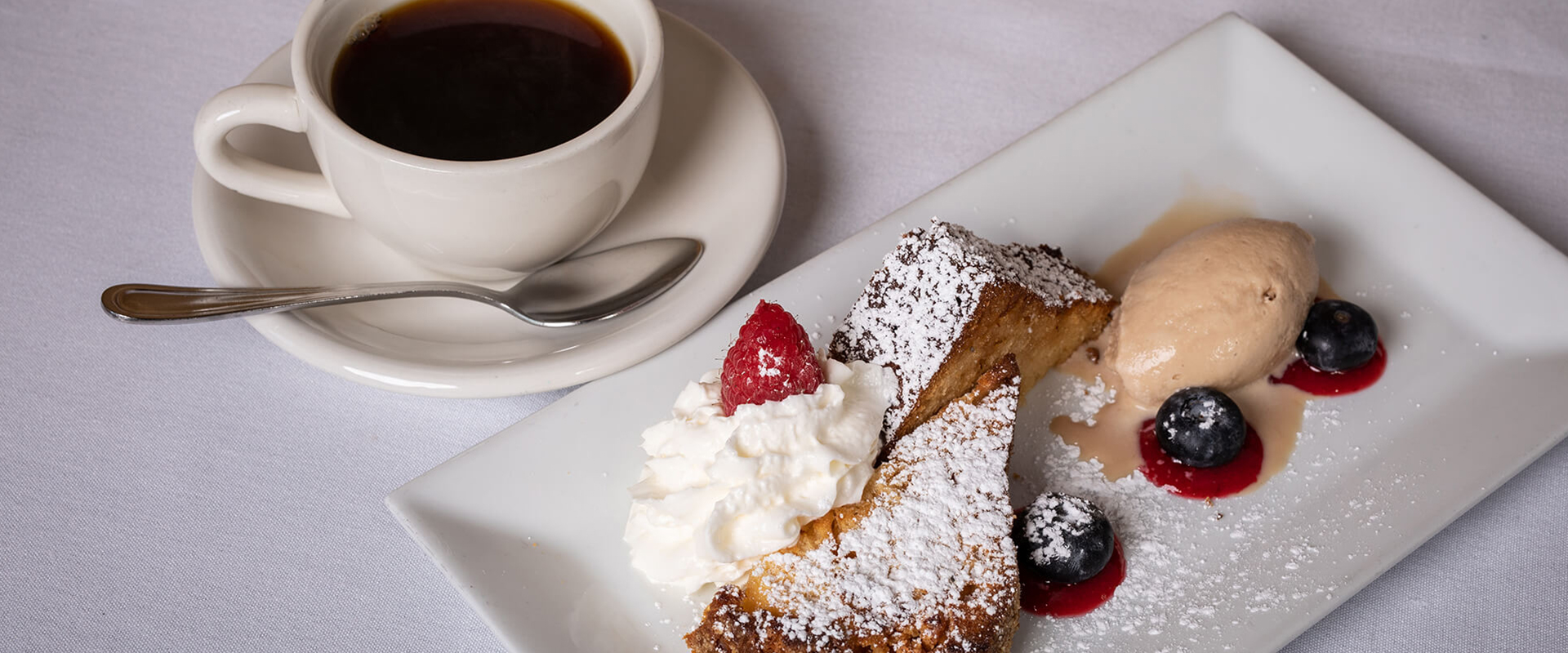 coffee next to a dessert plate with ice cream and berries